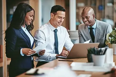 2 men and a woman sitting and looking at laptop in business attire